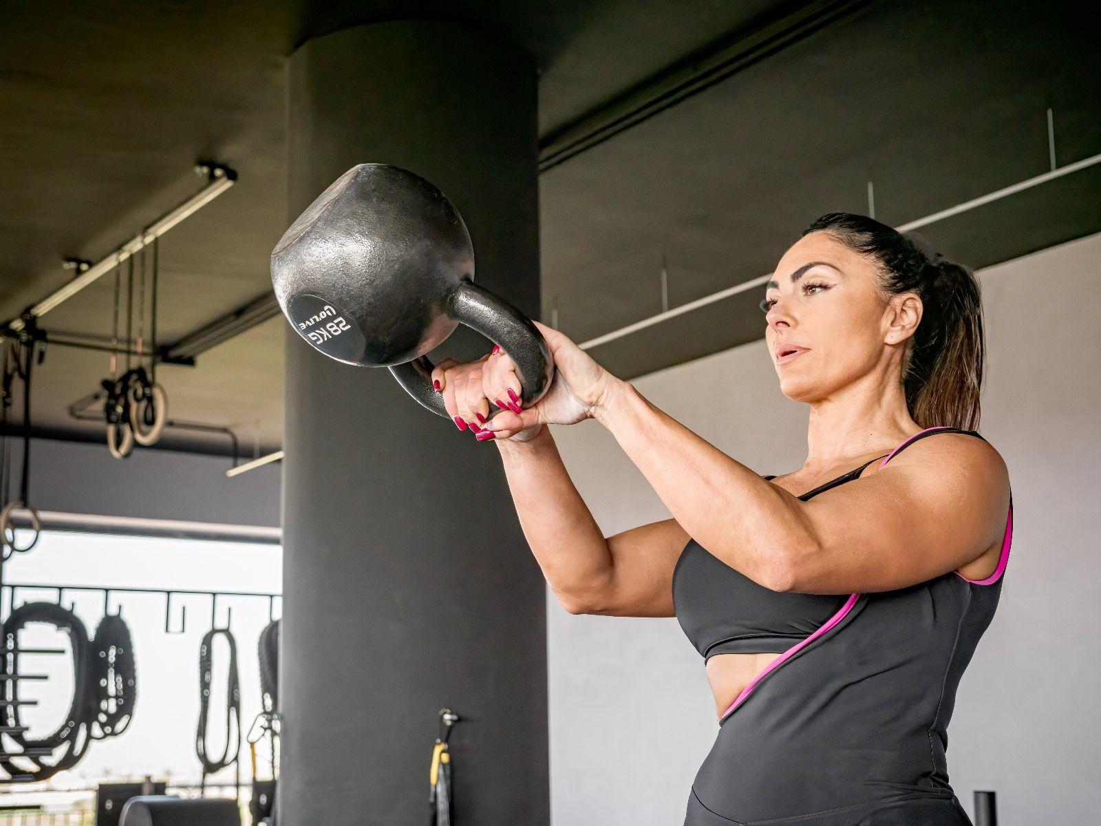 A woman in workout attire lifting a heavy kettlebell in a gym setting.