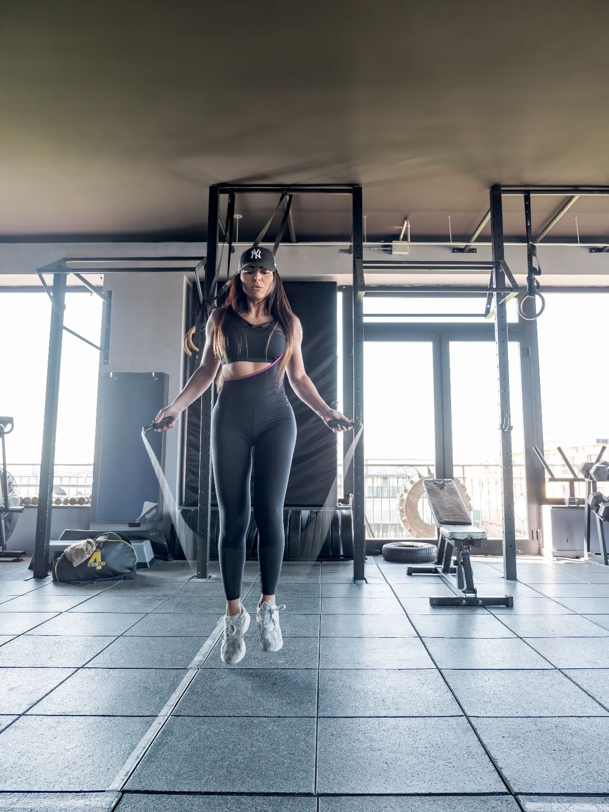 Person in athletic wear jumping rope inside a gym with various exercise equipment.